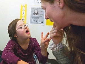 A woman working with a young girl on her sign language