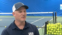 Tennis coach John Devorss sitting on a chair on a tennis court